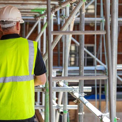 AW Associates LLP Building site with scaffolding and workman in hi vis jacket