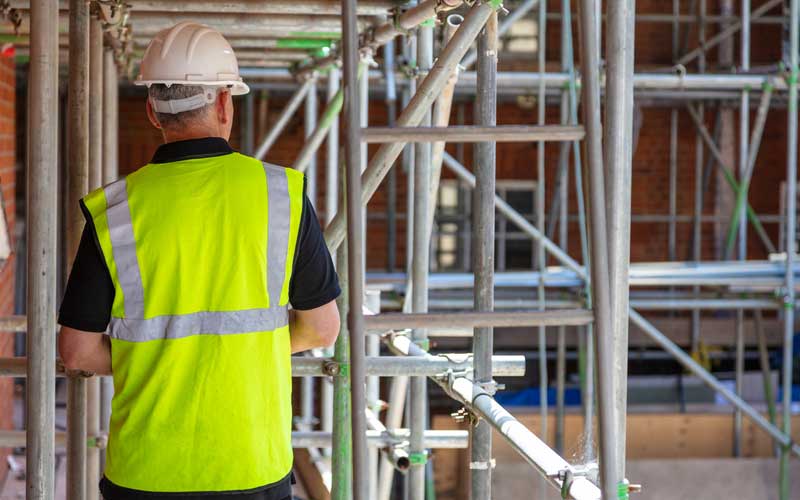 AW Associates LLP Building site with scaffolding and workman in hi vis jacket